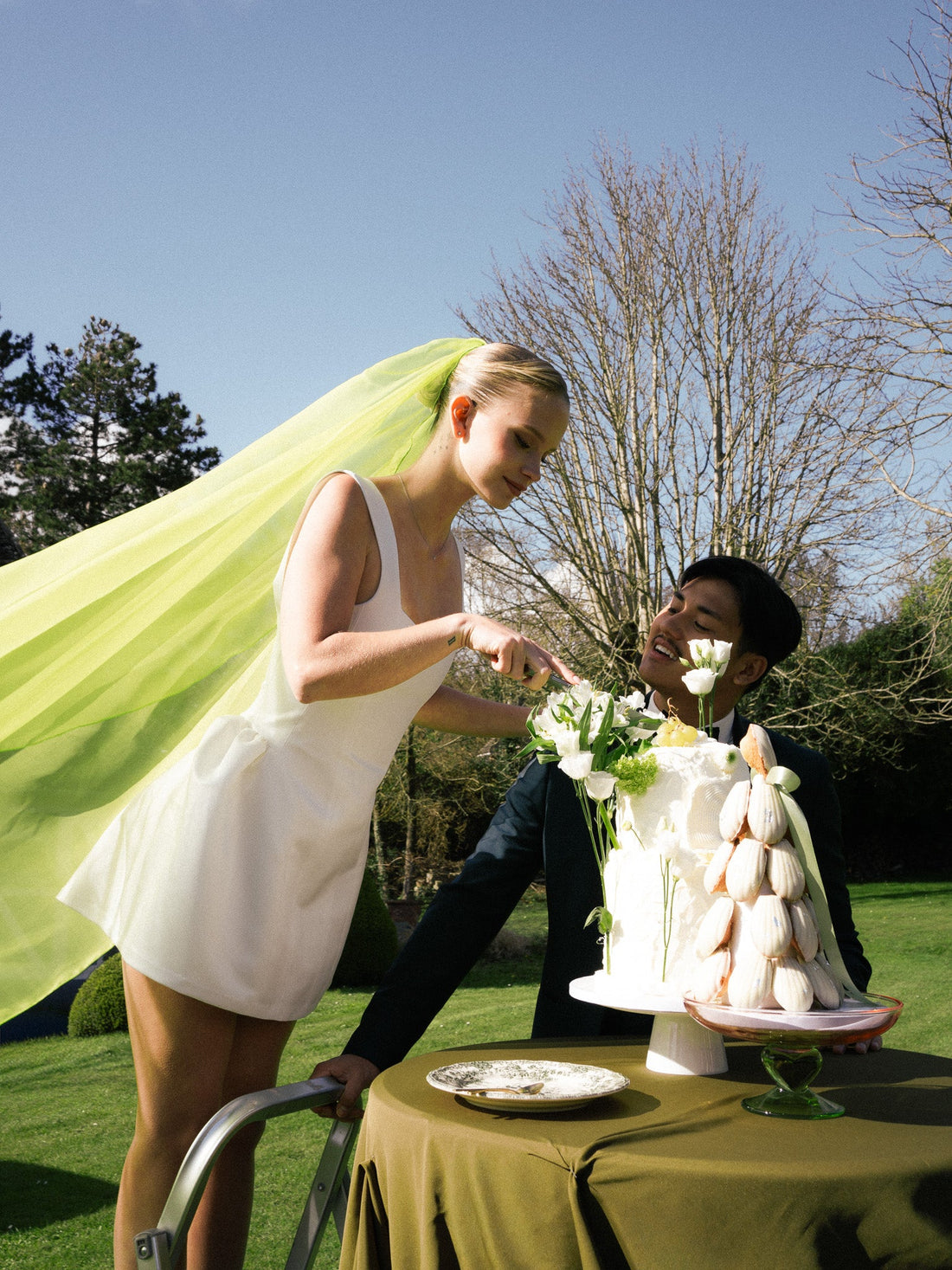 Mariée en robe courte blanche et voile vert chartreuse CANEZAN coupant le gâteau, pour un mariage coloré
