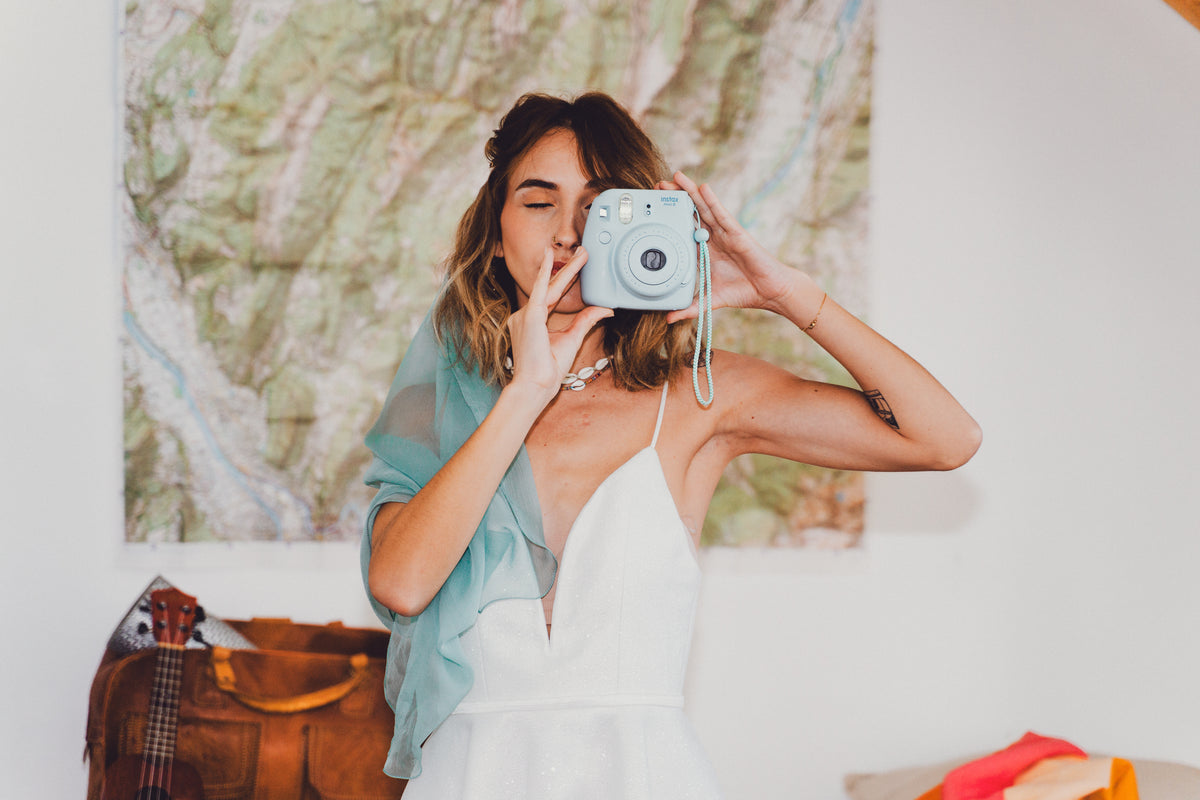 Mariée voyageuse avec un voile bleu lagon CANEZAN sur les épaules, prenant une photo devant une carte de randonnée